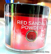 Red Sandalwood powder in a bowl with sandalwood sticks beside it.